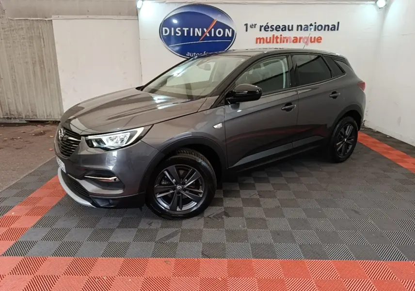 Opel Grandland X gris foncé en 3/4 avant droit, avec jantes noires et phares LED allumés, en intérieur showroom.