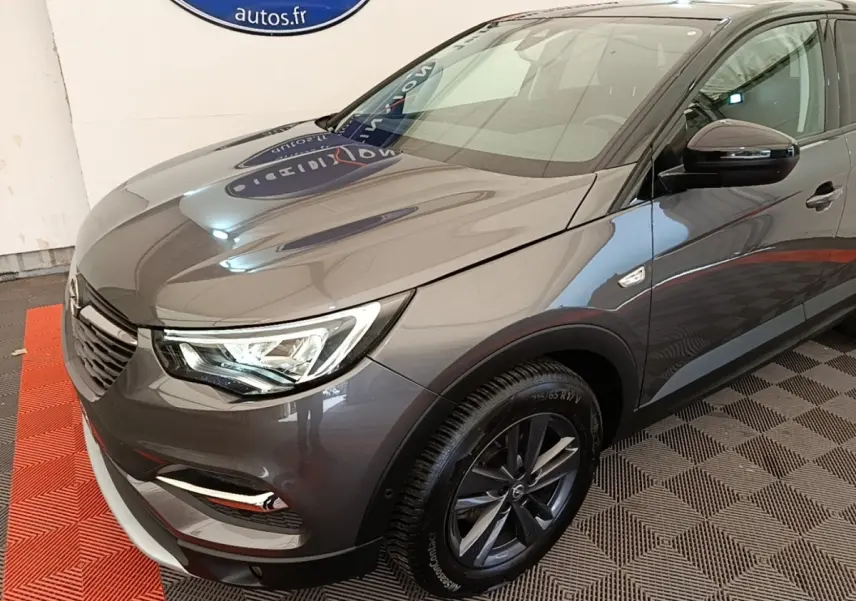 Vue 3/4 avant droit d'un Opel Grandland X gris foncé avec jantes alliage et phares LED visibles en intérieur showroom.