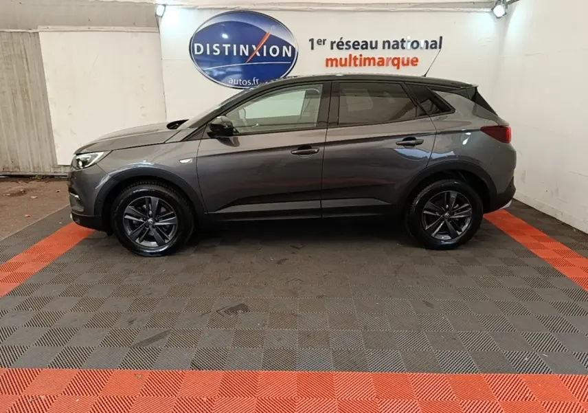 Profil côté gauche d'un Opel Grandland X gris foncé 2021 garé en intérieur avec jantes noires et toit noir.