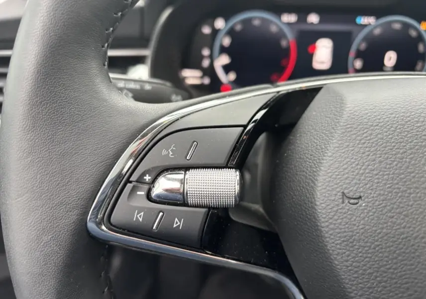 Gros plan sur le volant cuir à deux branches du Skoda Kamiq 2024, avec commandes audio et molette texturée côté gauche.