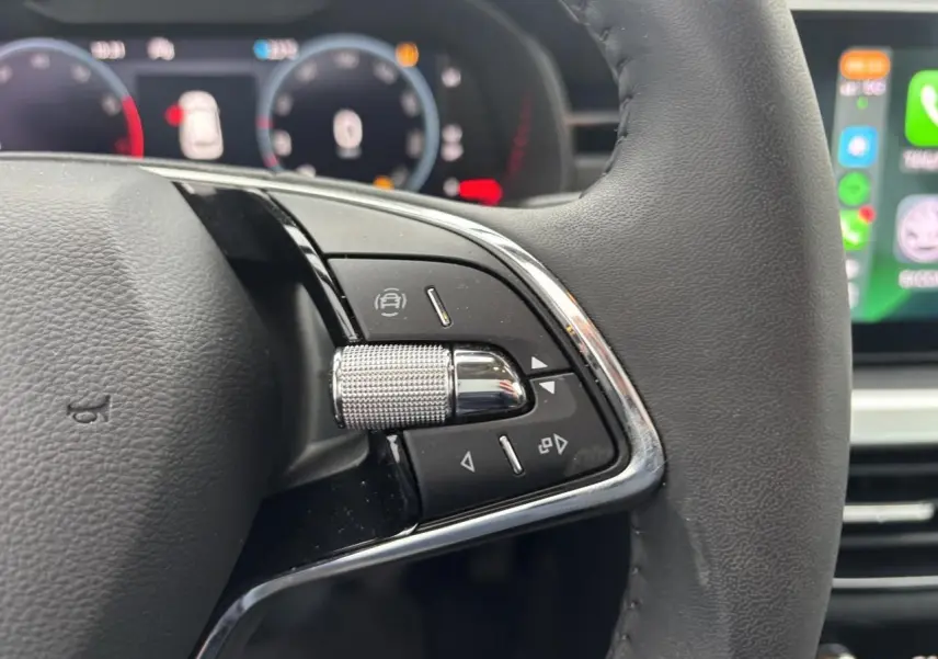 Gros plan sur le volant cuir 2 branches du Skoda Kamiq 2024, avec commandes multifonctions et tableau de bord numérique flou.