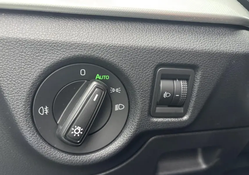 Gros plan sur la commande d’éclairage avec réglage automatique dans l’habitacle gris foncé du Skoda Kamiq 2024.