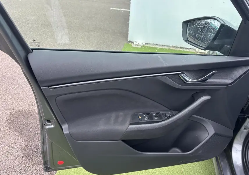 Porte avant gauche ouverte du Skoda Kamiq gris graphite, montrant les commandes des vitres et la poignée intérieure noire.