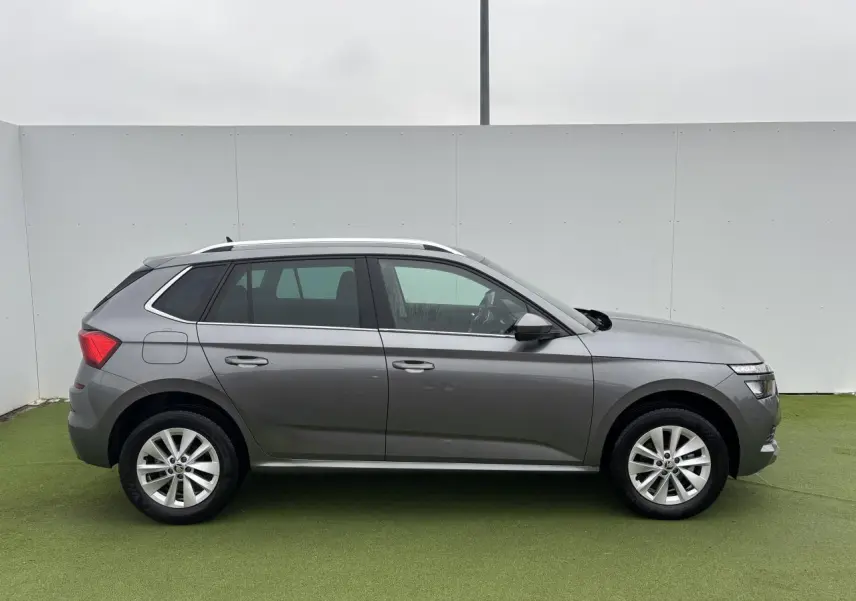 Profil droit d'un Skoda Kamiq gris graphite métallisé avec jantes alliage 17 pouces sur fond vert et mur blanc.