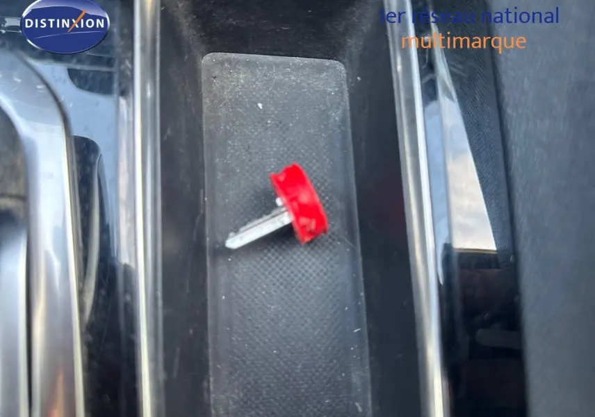 Gros plan sur la console centrale noire d’un Peugeot 3008 blanc nacré, avec une clé rouge posée dessus.