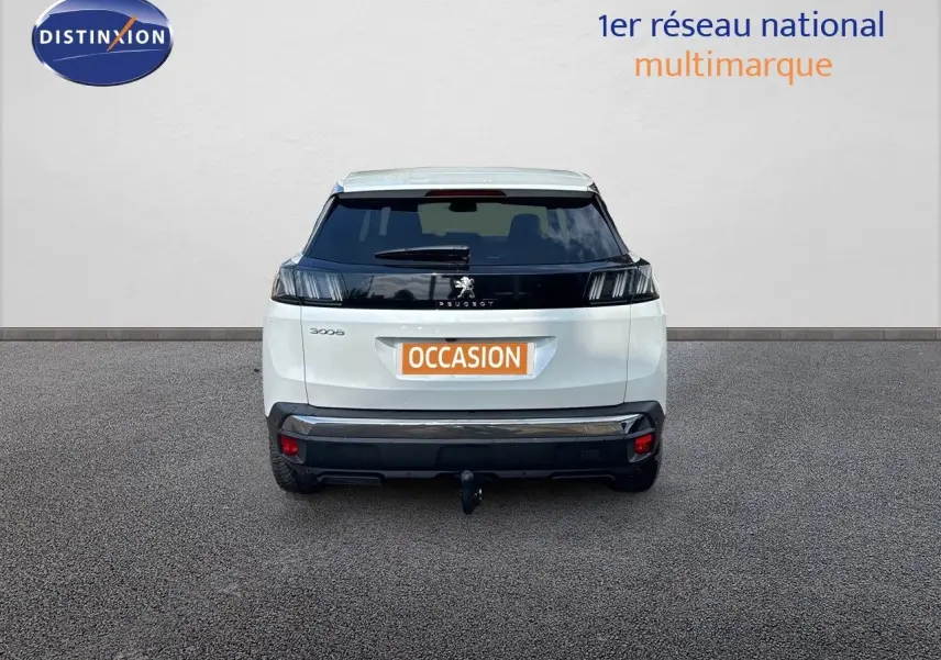 Vue arrière d'un Peugeot 3008 blanc nacré avec attelage, stationné devant un mur clair.