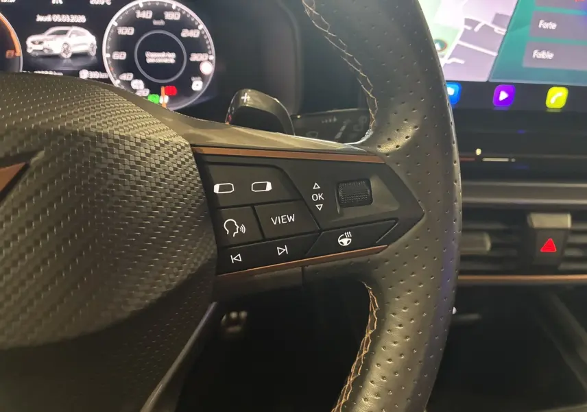 Gros plan sur le volant cuir perforé du CUPRA Formentor 1.4 e-Hybrid avec commandes multifonctions et écran numérique en arrière-plan.