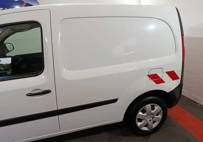 Vue latérale droite d’un Renault Kangoo blanc avec marquages rouges sur l’aile arrière et jantes argentées.