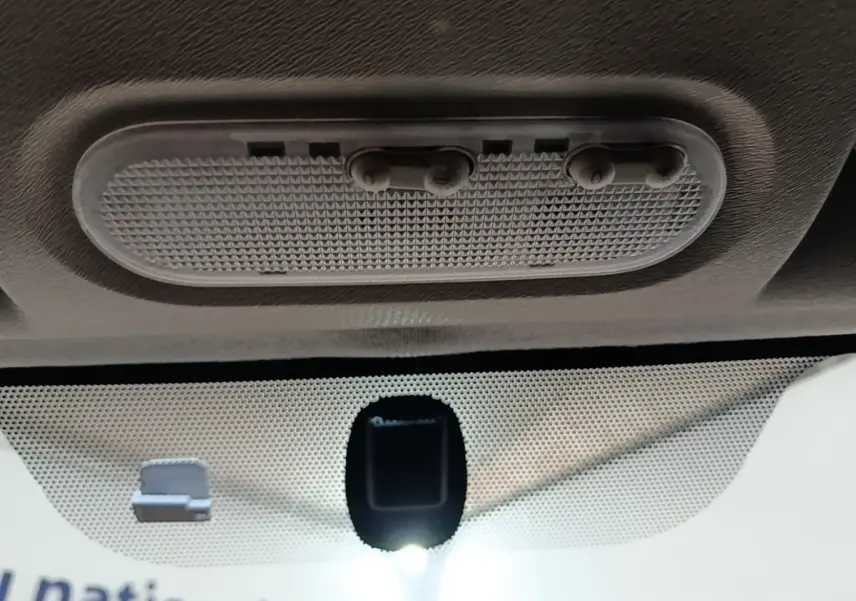 Vue intérieure en gros plan du plafonnier gris avec interrupteurs et capteur sur le pare-brise du Renault Kangoo blanc.