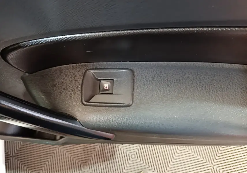 Gros plan sur le bouton de commande de la vitre électrique sur la porte intérieure noire d’un Renault Kangoo blanc.