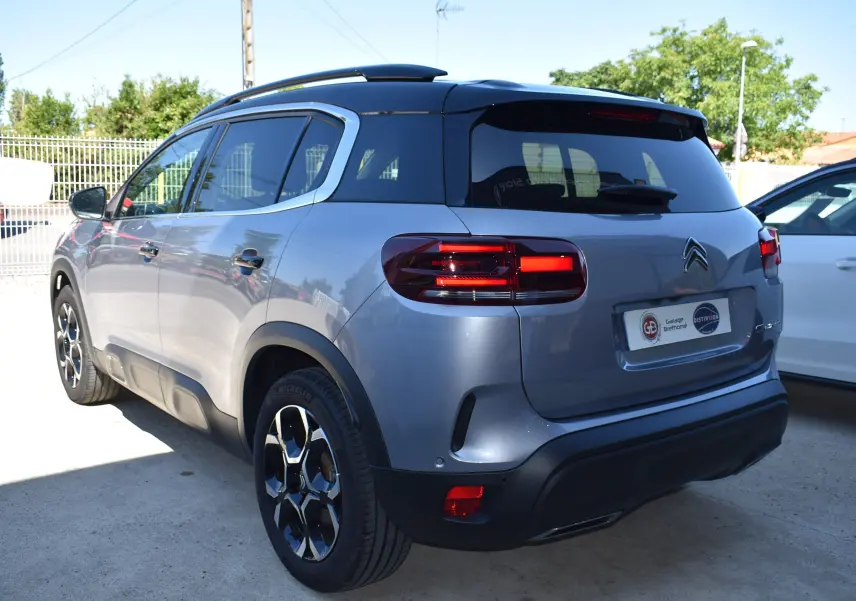 Vue 3/4 arrière droite du Citroën C5 Aircross 2024 gris métallisé avec toit bi-ton noir et feux arrière allumés.