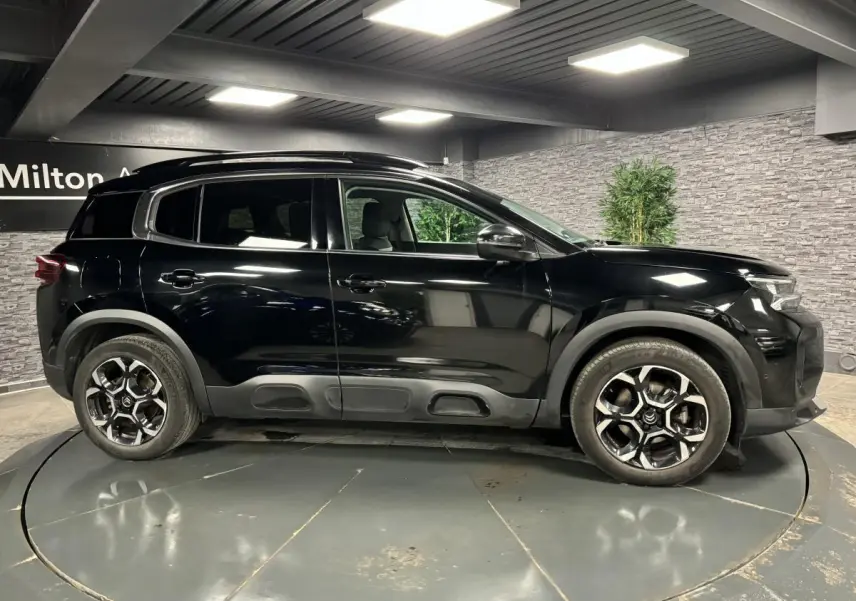Profil côté gauche d'un SUV Citroën C5 Aircross noir nacré avec jantes alliage bi-ton et barres de toit noires.