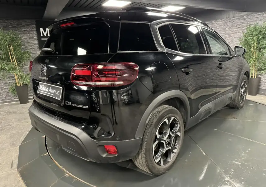 Vue 3/4 arrière droite du SUV Citroën C5 Aircross noir nacré avec jantes alliage bi-ton et barres de toit noires.