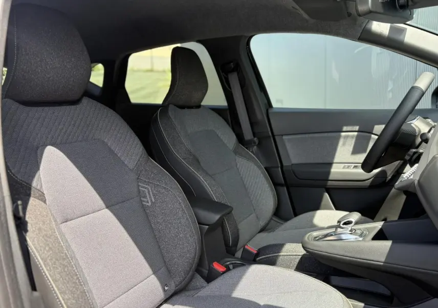 Intérieur du Renault Captur 2025 en vue latérale droite, sièges tissu gris avec console centrale et volant multifonctions.