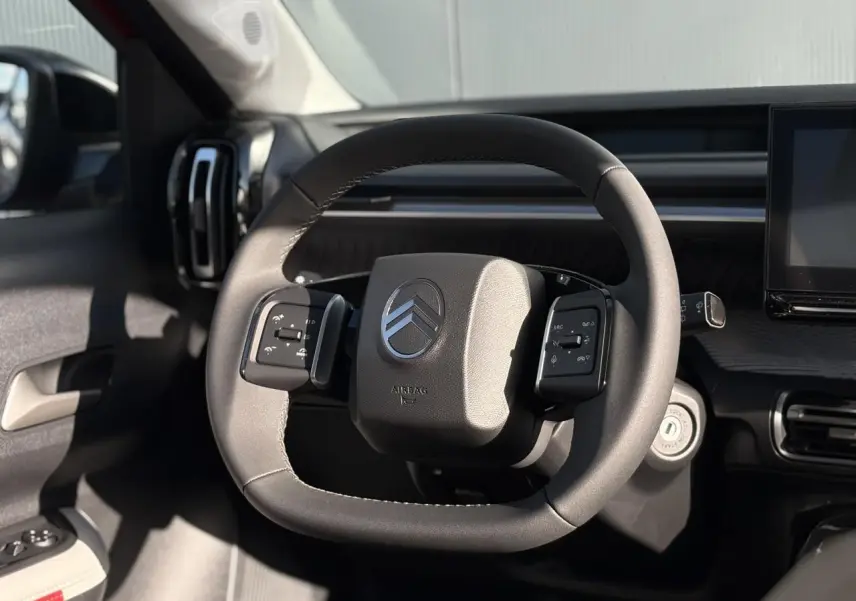 Volant multifonctions Citroën vu de face dans l'habitacle sombre, avec tableau de bord et écran tactile partiellement visibles.