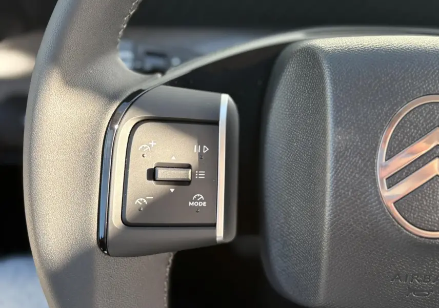 Gros plan sur les commandes multifonctions à gauche du volant noir du Citroën C3 Aircross Hybrid 2025.