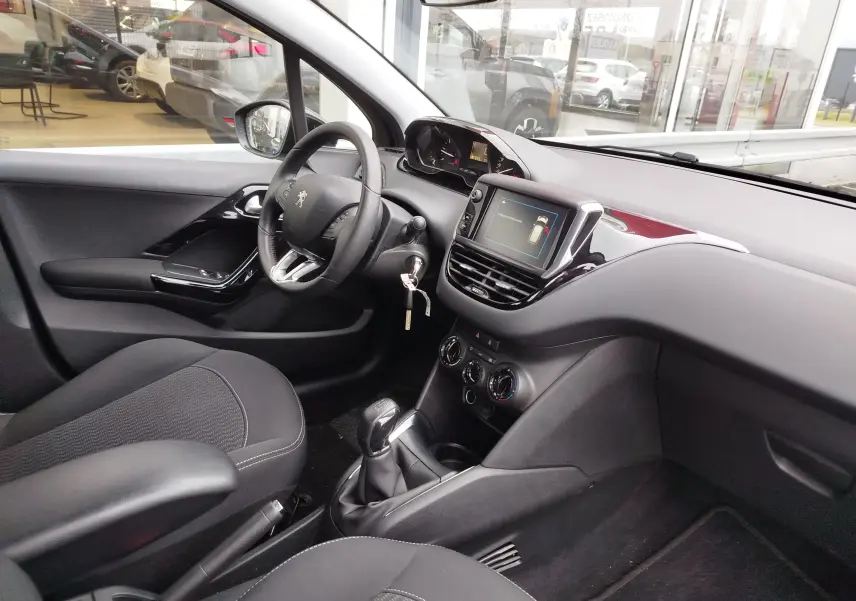 Vue intérieure côté conducteur de la Peugeot 208 noire, montrant le volant, la console centrale avec écran tactile et la boîte manuelle.