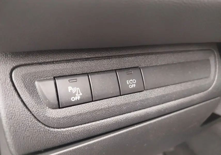 Gros plan sur les boutons de commande du tableau de bord noir de la Peugeot 208 Diesel, avec fonction ECO et parking désactivée.