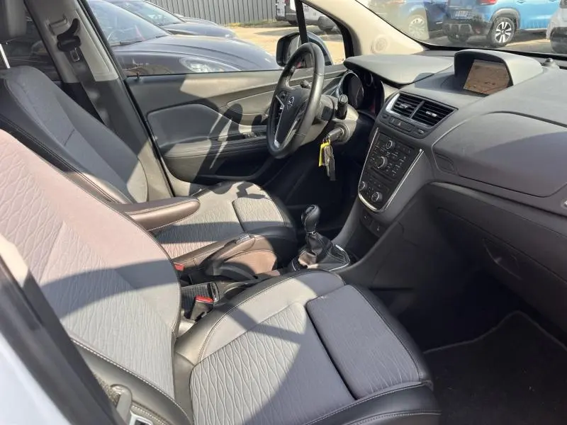 Intérieur de l’Opel Mokka blanc, vue côté conducteur, montrant les sièges gris et la console centrale avec boîte manuelle.