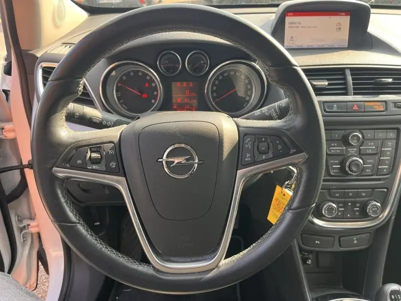 Vue intérieure centrée sur le volant cuir noir avec logo Opel, tableau de bord et écran multifonction en arrière-plan.