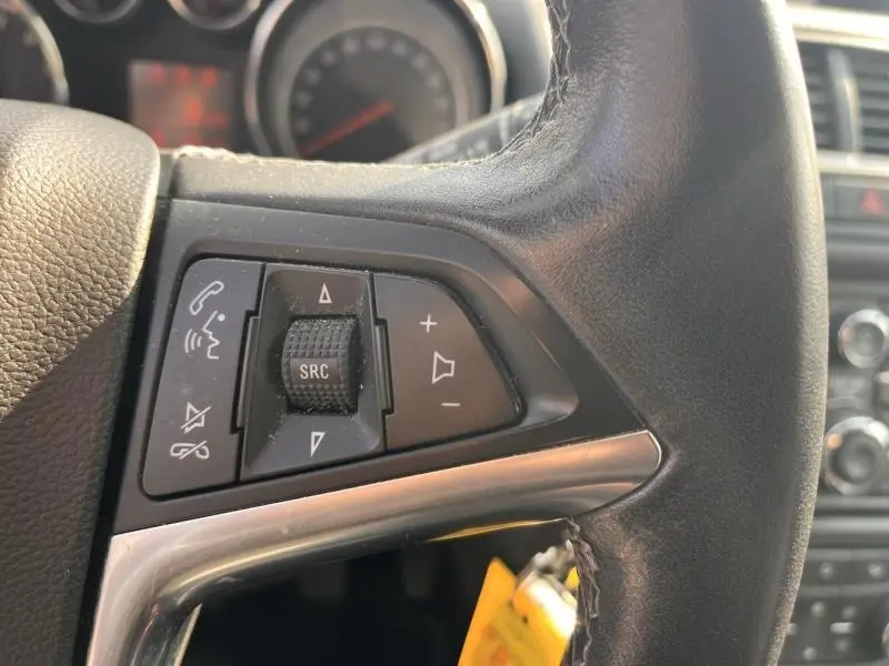 Gros plan sur les commandes multifonctions noires du volant cuir de l'Opel Mokka blanc, avec molette SRC et boutons volume.