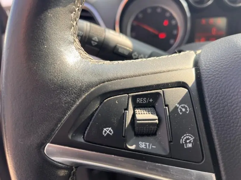 Gros plan sur les commandes de régulateur de vitesse au volant cuir noir de l’Opel Mokka blanc Glacier 2015.