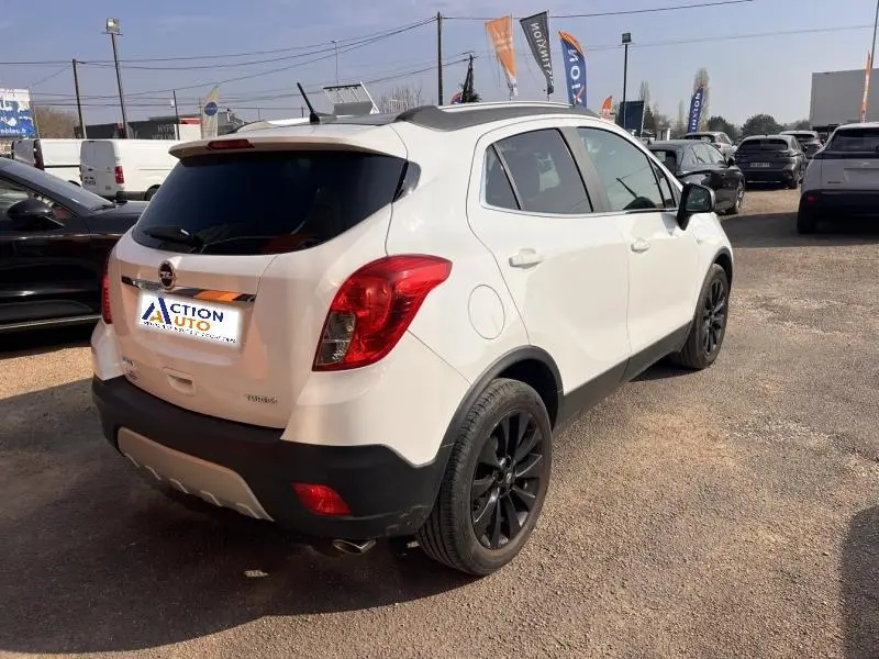 Vue 3/4 arrière droite d'un Opel Mokka blanc Glacier avec jantes noires et vitres teintées sur parking extérieur.