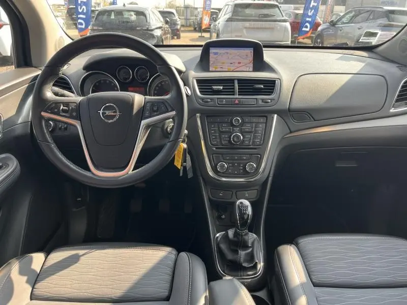 Vue intérieure avant de l'Opel Mokka 2015, tableau de bord noir avec écran GPS et volant multifonction cuir.