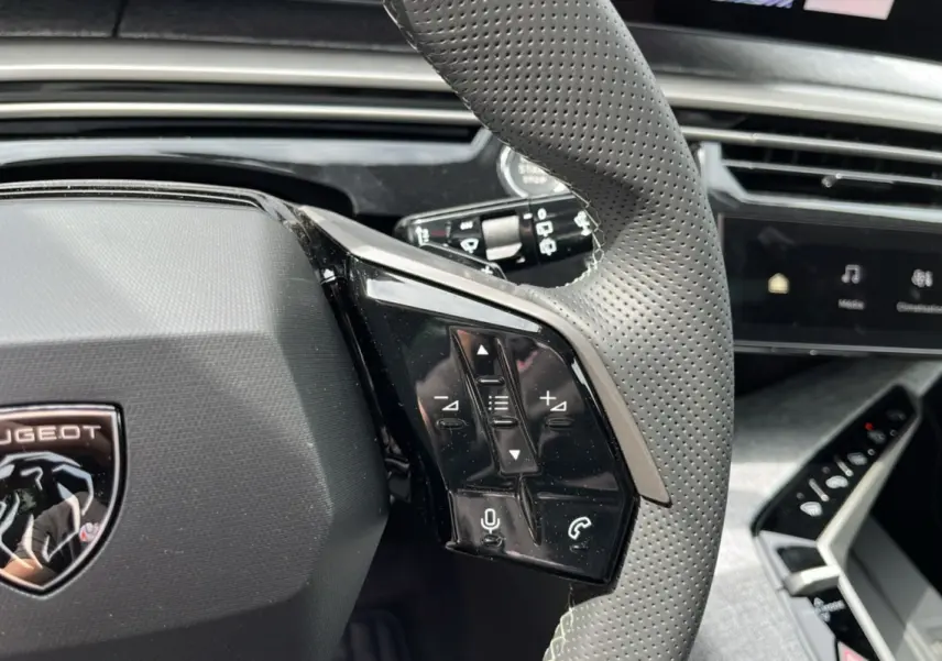 Gros plan sur le volant cuir perforé du Peugeot 5008 Hybrid 145 GT avec commandes multifonctions et logo lion.