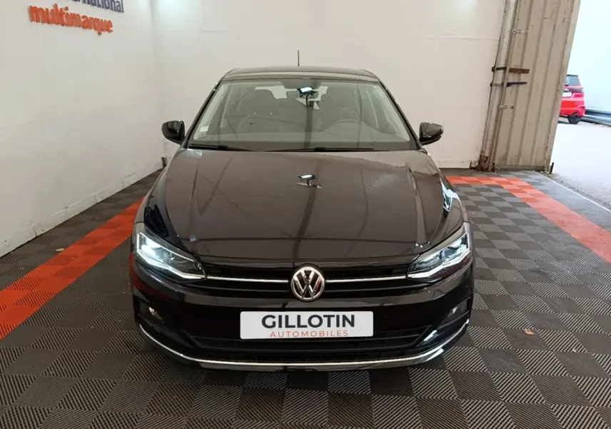 Vue avant d'une Volkswagen Polo noire 2020 avec phares LED allumés dans un garage intérieur.