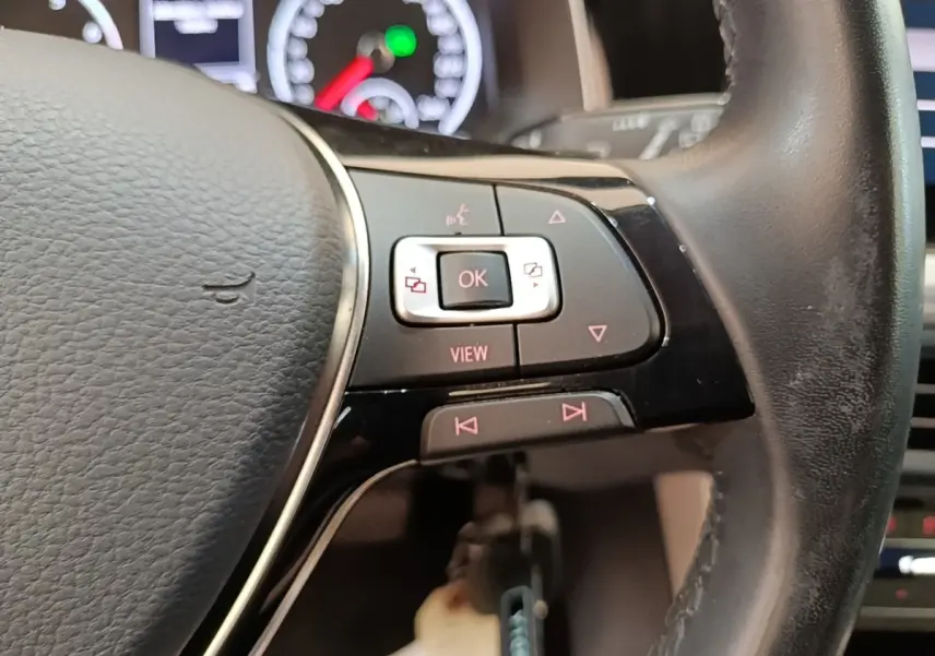 Gros plan sur le volant cuir noir de la Volkswagen Polo 2020, avec commandes multifonctions et tableau de bord en arrière-plan flou.
