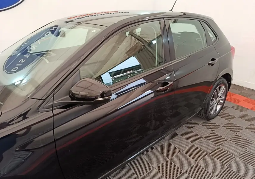 Vue latérale droite d'une Volkswagen Polo noire 2020, avec rétroviseur et poignées de porte visibles, sur sol à damiers.