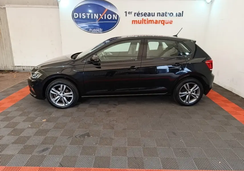 Profil côté gauche d'une Volkswagen Polo noire 2020, version Carat, sur sol damier gris et rouge en intérieur showroom.