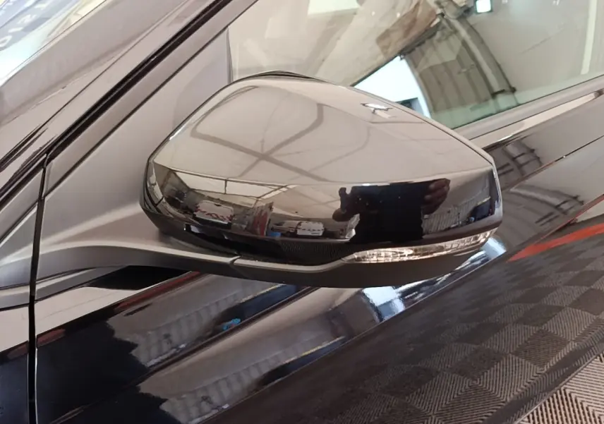 Rétroviseur côté gauche noir brillant de Volkswagen Polo 1.0 TSI 115 DSG7 Carat, reflet intérieur d'atelier visible.