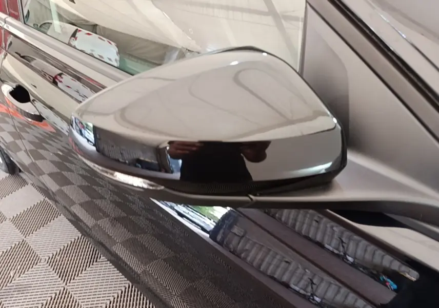 Gros plan sur le rétroviseur droit noir brillant d'une Volkswagen Polo 2020, reflet d'un garage intérieur.