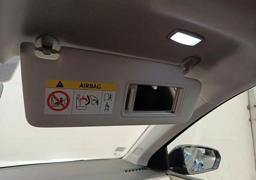 Vue intérieure côté passager du pare-soleil beige avec miroir et éclairage, rétroviseur extérieur noir visible.