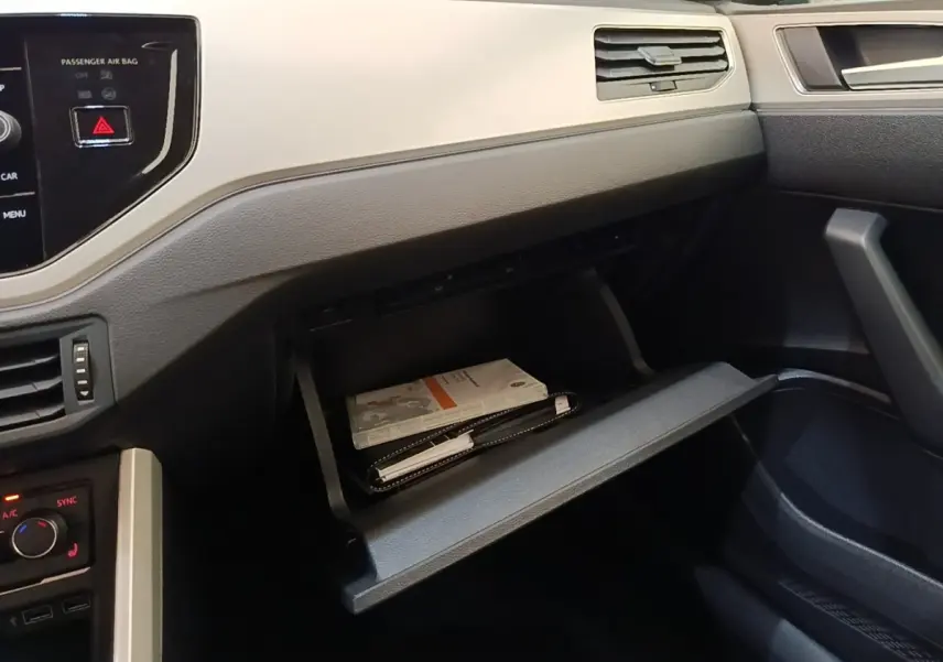 Vue intérieure côté passager de la Volkswagen Polo noire 2020, boîte à gants ouverte avec documents visibles.