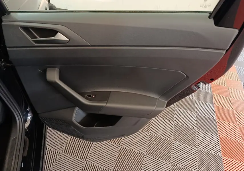 Vue rapprochée de la porte avant gauche noire d’une Volkswagen Polo 1.0 TSI 115 DSG7 Carat avec poignée intégrée.