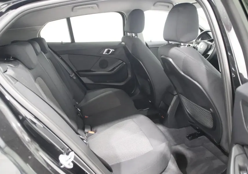 Vue intérieure côté gauche des sièges arrière noirs en tissu d'une BMW Série 1 116d 2023 avec porte ouverte.