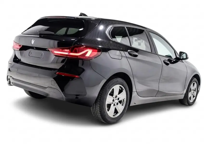 BMW Série 1 116d noire vue en 3/4 arrière droit, avec feux arrière allumés et jantes alliage cinq branches.