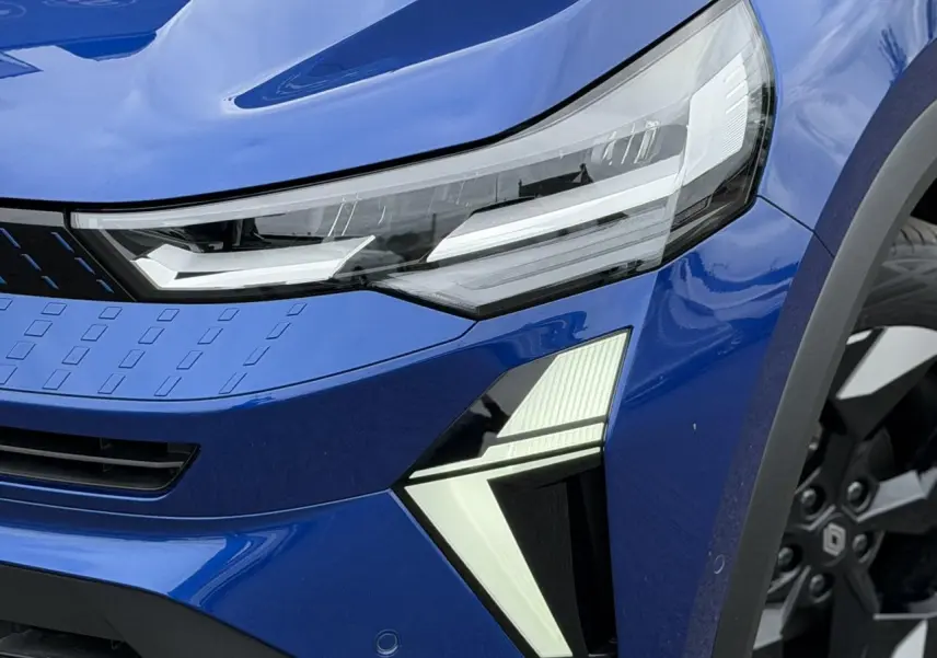Gros plan sur l'avant droit bleu Iron du Renault Captur 2026, mettant en valeur les phares LED et la jante aluminium noire.