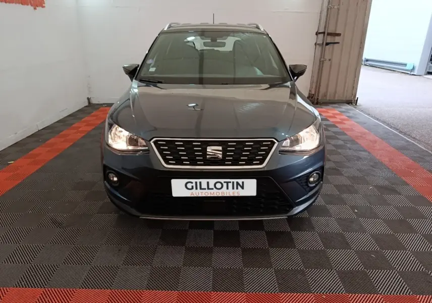 Vue avant d'un SEAT Arona gris clair avec calandre chromée et phares allumés dans un garage.
