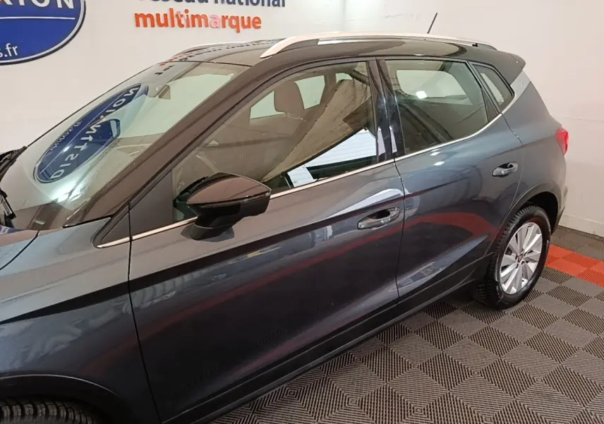 Vue latérale droite d'un SEAT Arona gris clair 2019, avec rétroviseur noir et jantes argentées, en intérieur showroom.