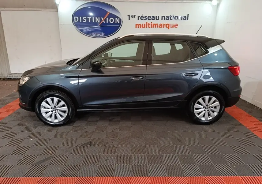 Vue latérale droite d'un SEAT Arona gris foncé stationné en intérieur avec jantes argentées et toit noir.