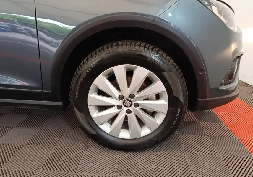 Gros plan sur la roue avant droite d’un SEAT Arona gris clair, avec jante alliage et logo central visible.