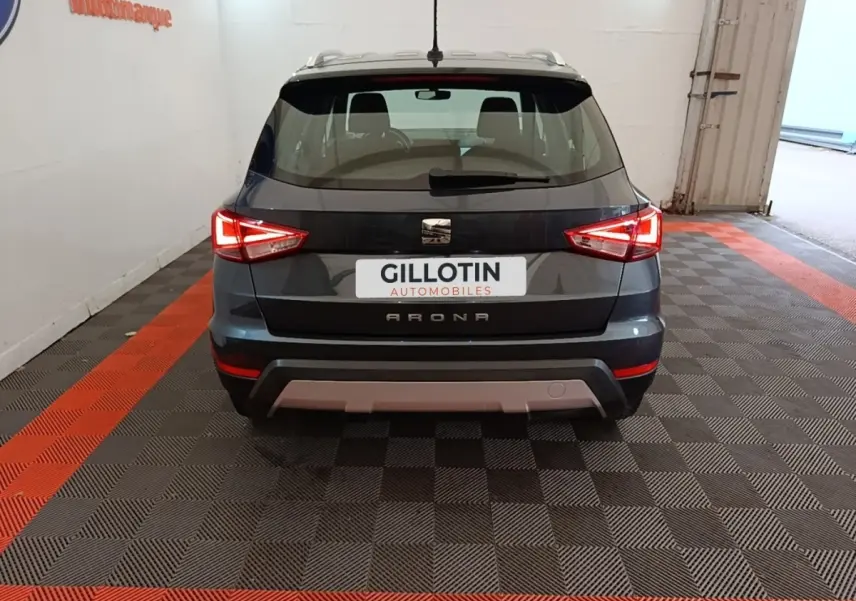 Vue arrière d'un SEAT Arona gris clair avec feux arrière allumés dans un garage au sol damier noir et rouge.