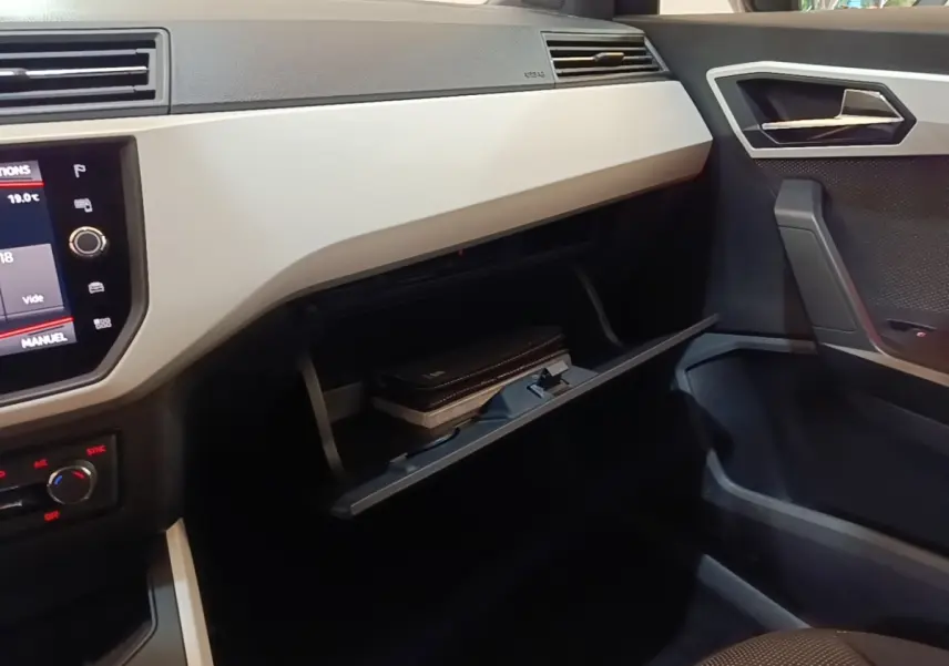 Intérieur côté passager du SEAT Arona 2019, tableau de bord clair avec boîte à gants ouverte et écran tactile visible.