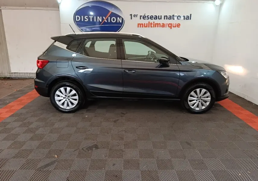 Vue latérale droite d'un SEAT Arona gris clair 2019 garé en intérieur avec jantes argentées et toit noir.