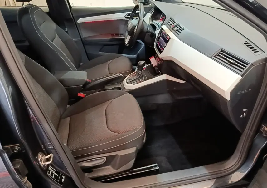 Vue intérieure côté conducteur du SEAT Arona 2019, sièges tissu gris foncé et tableau de bord clair avec écran tactile.