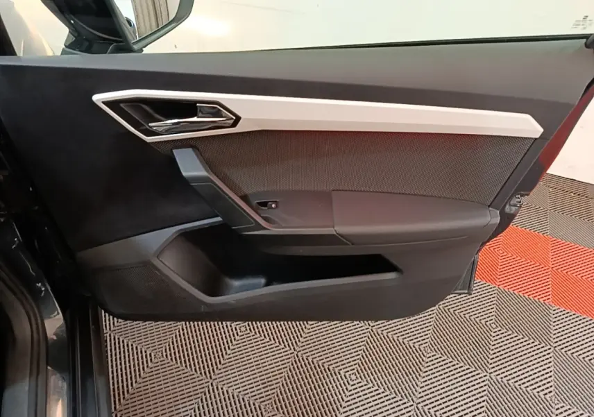 Vue rapprochée de la porte avant gauche d'une SEAT Arona gris clair, avec poignée chromée et garniture noire.